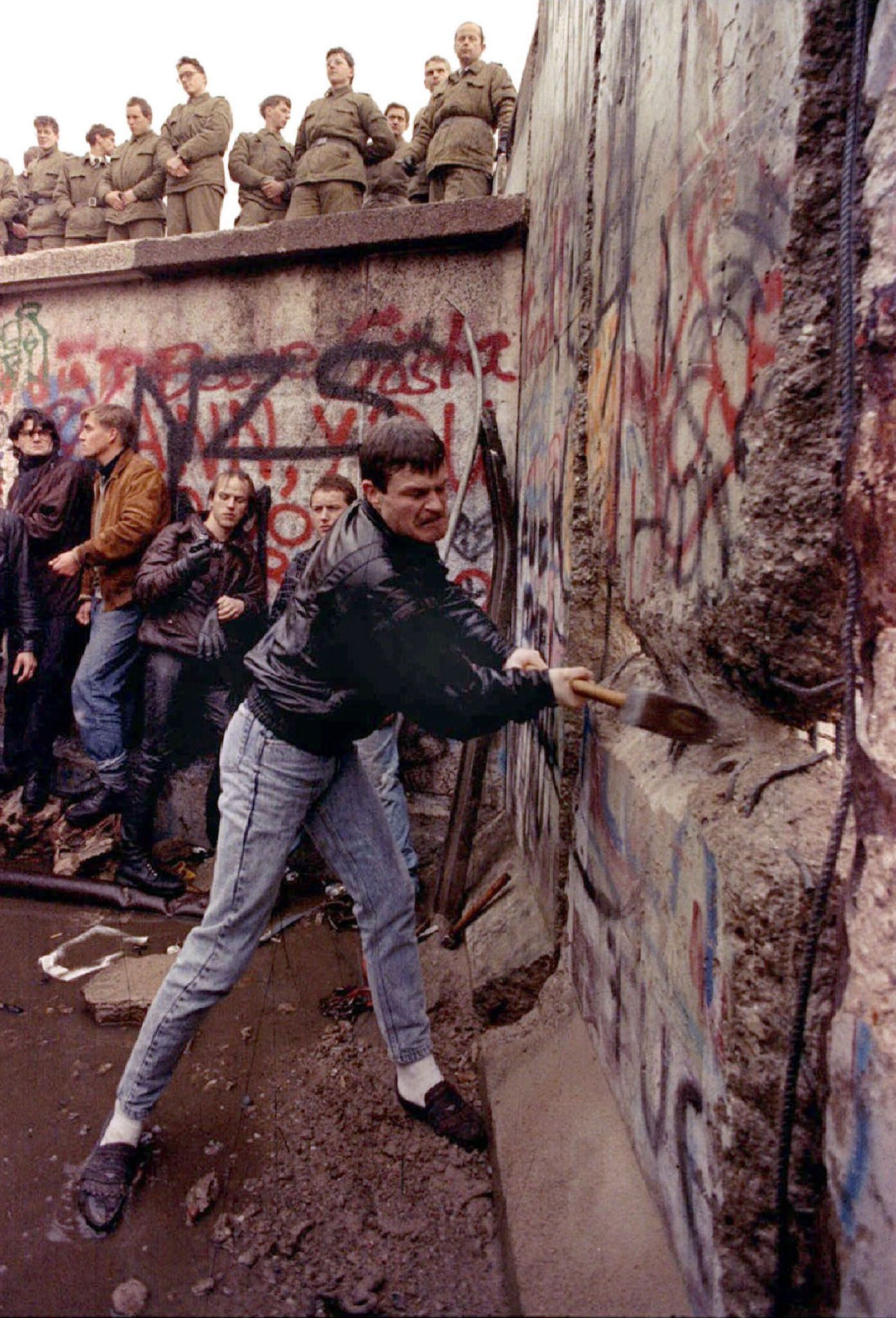 Ein Demonstrant hämmert gegen die Berliner Mauer, während ostdeutsche Grenzsoldaten von oben am Brandenburger Tor zusehen, 11. November 1989.