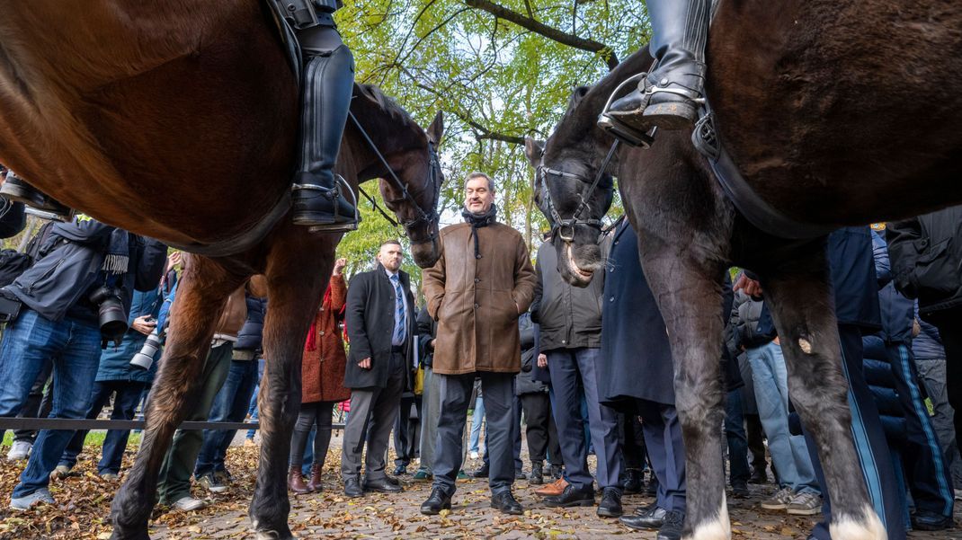 Markus Söder (CSU), Ministerpräsident von Bayern, steht im Alten Botanischen Garten zwischen zwei berittenen Polizisten.