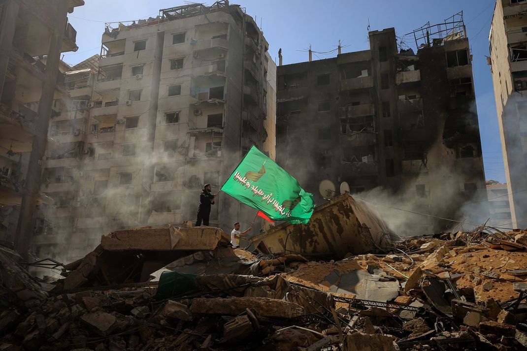 Pro-iranische Hisbollah-Anhänger schwenken Fahnen, während sie auf den Trümmern der zerstörten Gebäude stehen, die bei einem israelischen Luftangriff auf einen südlichen Vorort von Beirut zerstört wurden.