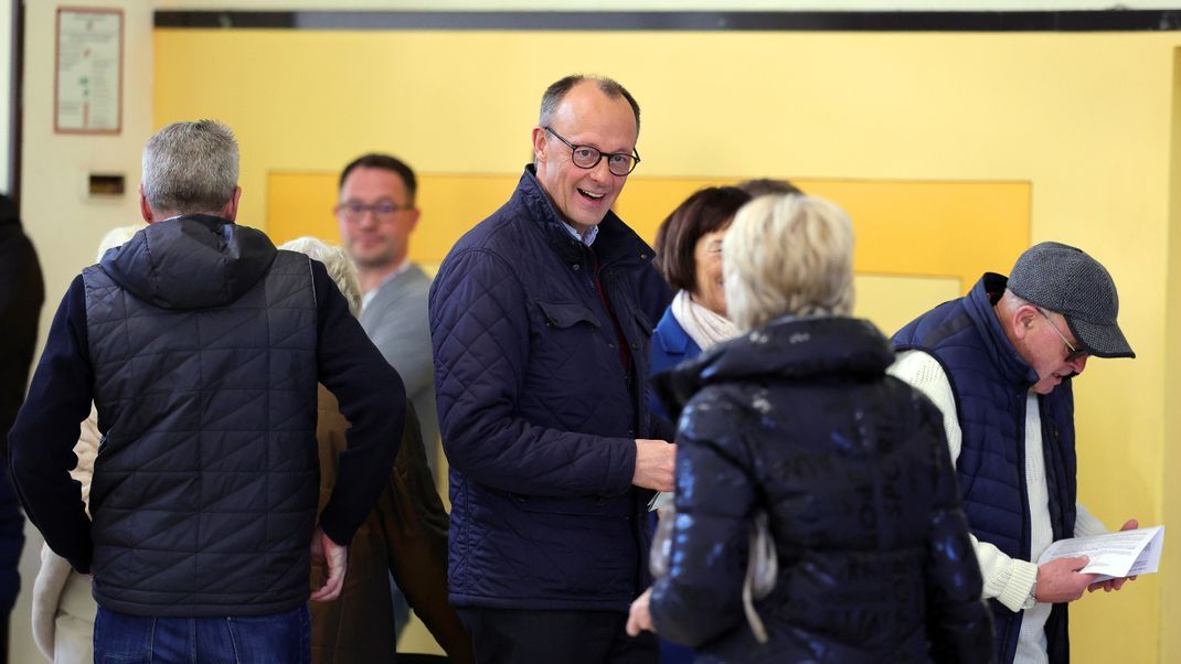 23. Februar 2025, Nordrhein-Westfalen, Arnsberg: Friedrich Merz, CDU-Parteivorsitzender und Kanzlerkandidat der Union, unterhält sich bei der Stimmabgabe im Wahllokal in der Schützenhalle Arnsberg-Niedereimer mit einer Bürgerin. 