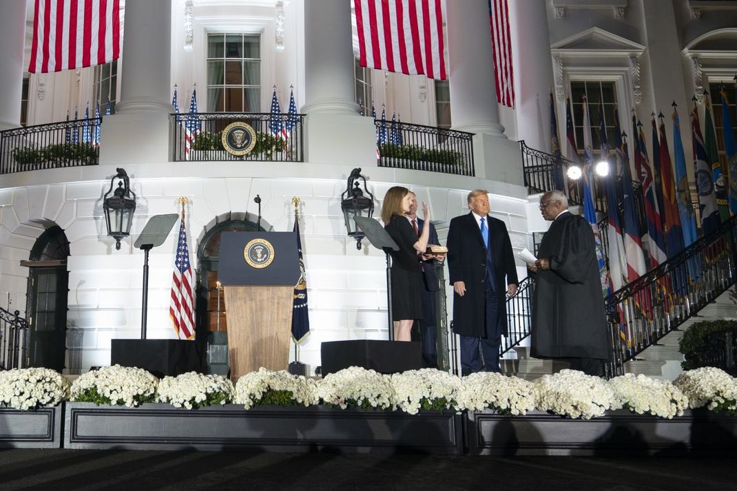 Auf dem Foto siehst du, wie Amy Coney Barrett am 26. Oktober 2020 im Beisein von US-Präsident Donald Trump am Weißen Haus als Richterin für den Supreme Court vereidigt wird.