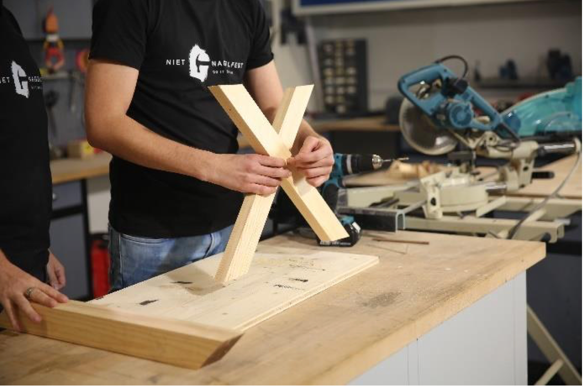 Im nächsten Schritt entfernen Sie die Holzstücke aus der Schraubzwinge und legen Sie kreuzförmig übereinander. Dort soll das Loch für die Gewindestange entstehen. Dafür markieren Sie die Schnittflächen der beiden Latten und bohren ein Loch durch die Mitte, dass so dick ist, das die Gewindestange hindurchpasst.