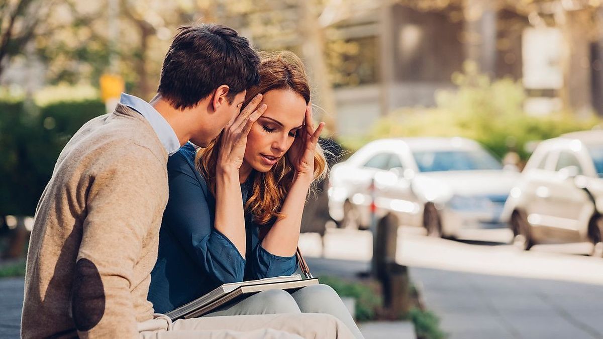 Couple sitting outdoors with woman holding head in hands