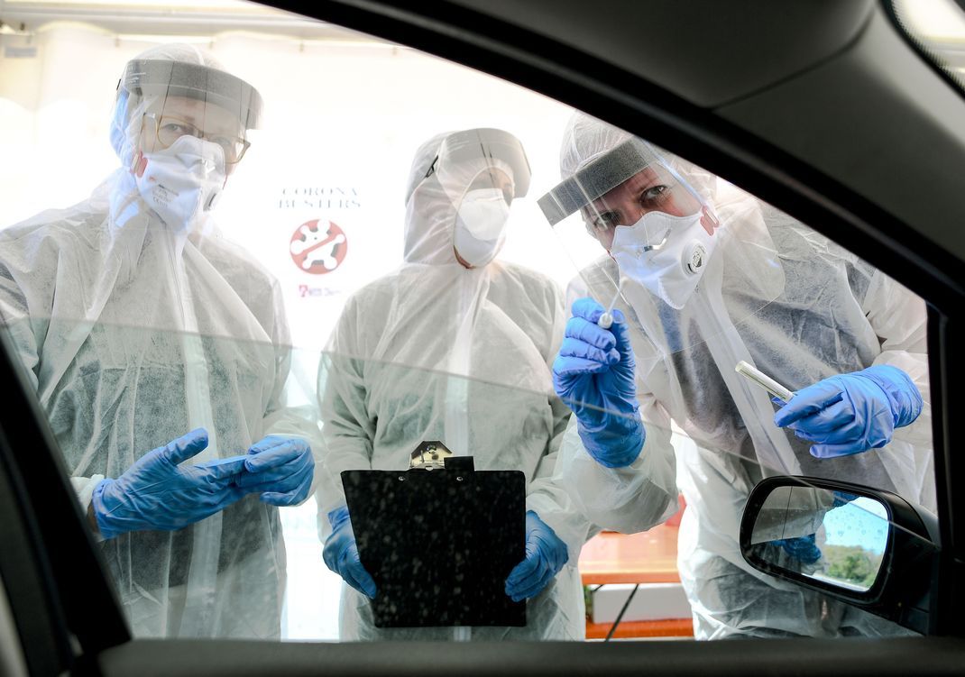 Mitarbeiter:innen vom Gesundheitsamt halten ein Abstrichstäbchen in ein Autofenster in der ambulanten Corona-Test-Einrichtung. (Symbolbild)