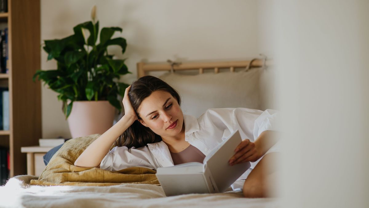 Beautiful woman reading book in bed, cozy, warm and contented feeling. Freedom in story, weekend activity for single woman.