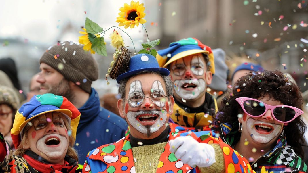 Besucher in Clown-Kostümen werfen in Nürnberg beim Faschingsumzug mit Konfetti.