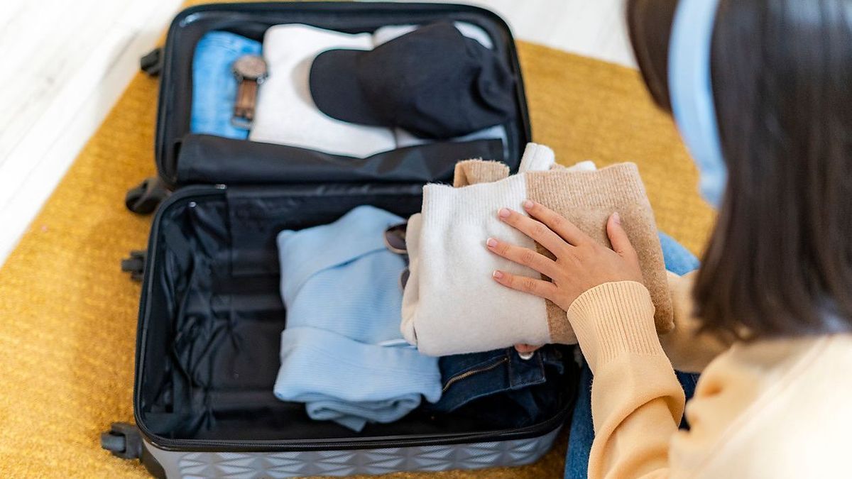 Young woman packing clothes in luggage at home