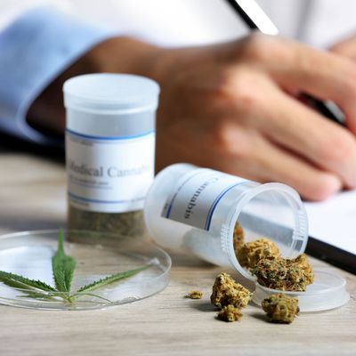 Doctor writing on prescription blank and bottle with medical cannabis on table close up