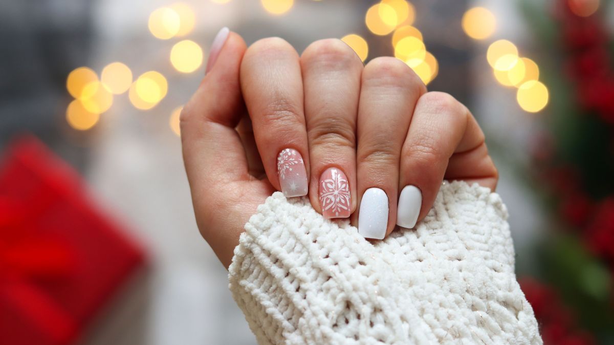 Idea of the winter manicure. Woman's hand with gel polish manicure white color and with snowflakes ornament against festive Christmas background. Selective focus