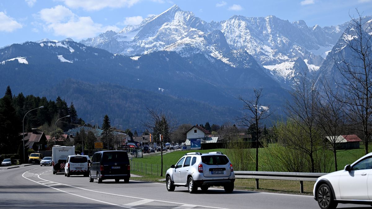 Autos fahren vor der Bergkulisse in den Ort rein. Dabei kommt es zum Stau am Ortseingang. 