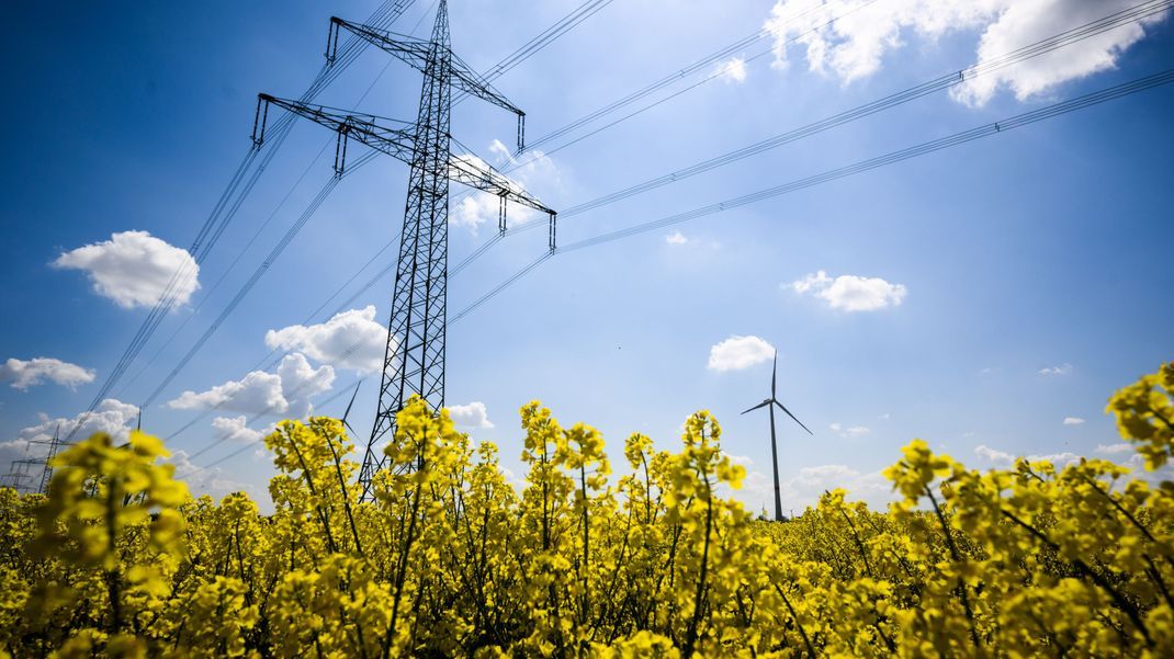 Niedersachsen, Hohenhameln: Windräder und eine Hochspannungsleitung stehen hinter einem Rapsfeld im Landkreis Peine.