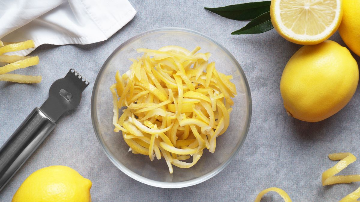 Zester, fresh lemons and bowl with pieces of peel on grey table, flat lay