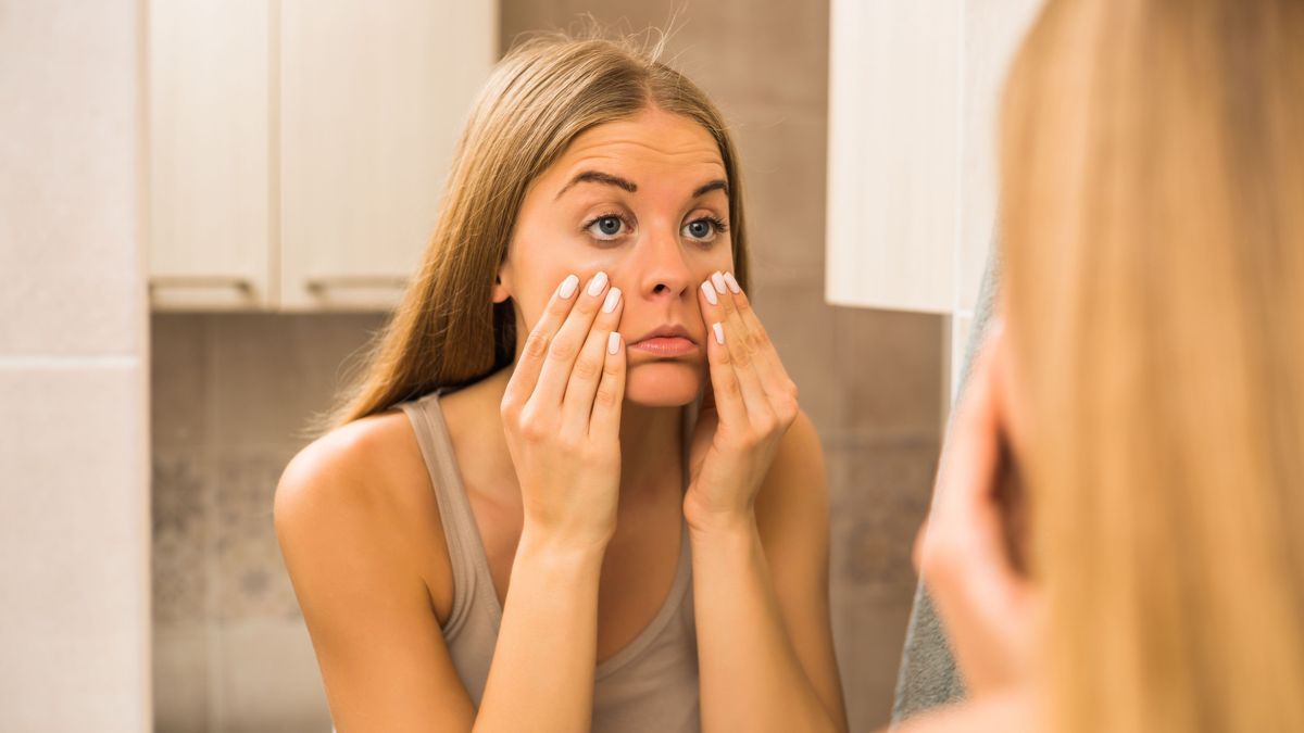 Tired woman looking her eye bags in the bathroom.