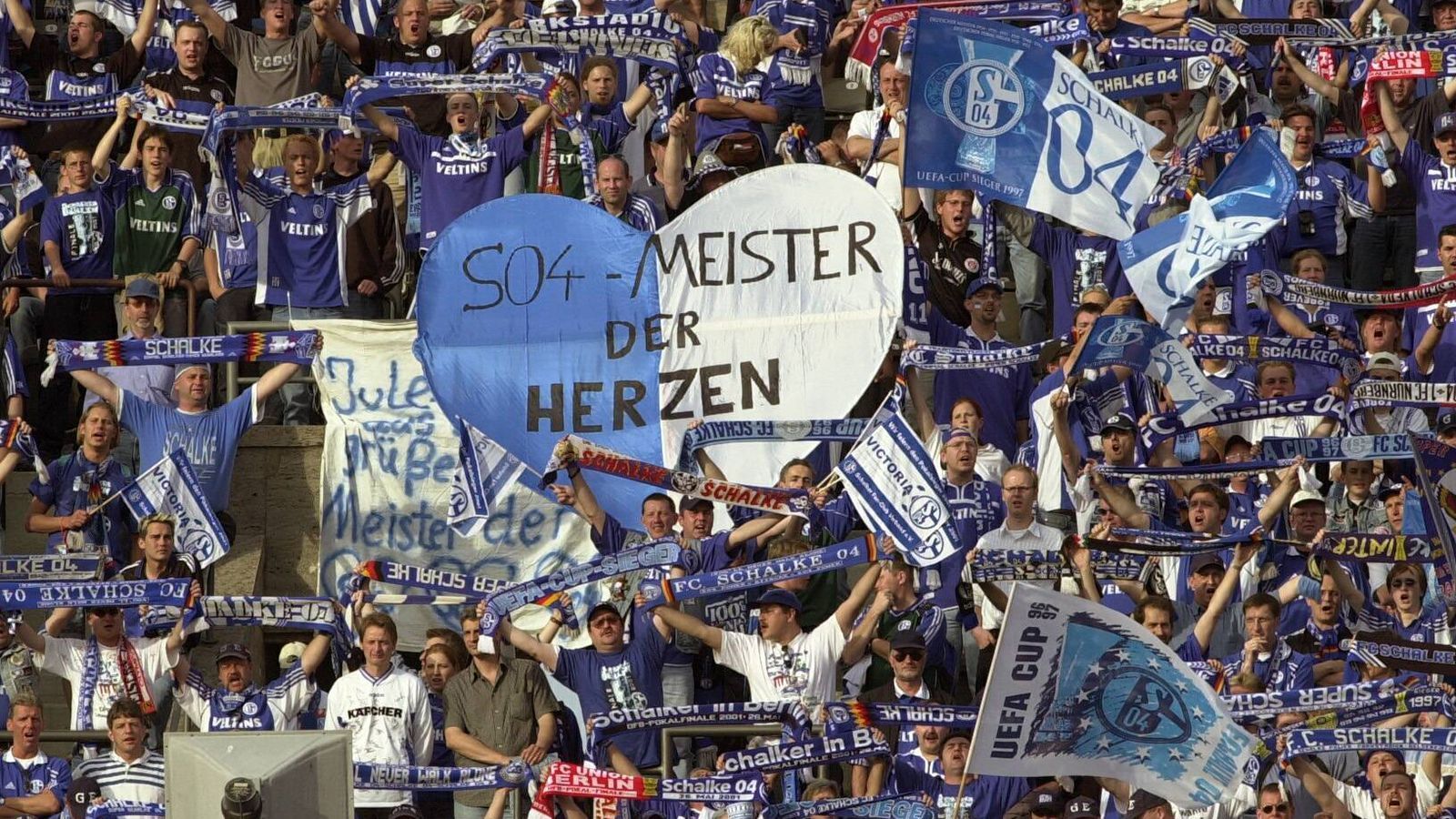 
                <strong>2000/01: Die Geburt der "Meister der Herzen"</strong><br>
                Seit der Bundesliga-Gründung wartet der FC Schalke 04 auf einen Meistertitel. Am 19. Mai 2001 fährt Königsblau dann Achterbahn. Eigentlich ist der FC Bayern fast schon durch. Schalke verliert am 33. Spieltag in Stuttgart, die Münchener gehen mit drei Punkten Vorsprung ins letzte Spiel. Einzige Hoffnung für S04: das bessere Torverhältnis. Schalke erledigt seine Aufgabe gegen die SpVgg Unterhaching und gewinnt mit 5:3. Parallel spielt der FC Bayern in Hamburg. Bis zur 90. Minute steht es 0:0, Bayern wäre Meister. Doch dann kommt Sergej Babarez und bringt den HSV in Front. Schalke ist genau für vier Minuten Meister, dann pfeift Schiedsrichter Markus Merk einen umstrittenen Rückpass der Hamburger. Patrik Andersson knallt den Freistoß in den Kasten und am Ende holen sich doch wieder die Bayern die Schale. Auf Schalke bricht blankes Entsetzen aus.
              