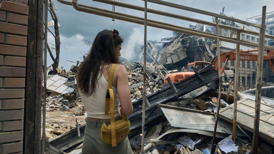 Ukraine, Odessa: Eine Frau sieht zu, wie Rettungskräfte nach einem Angriff an einem zerstörten Gebäude arbeiten. 