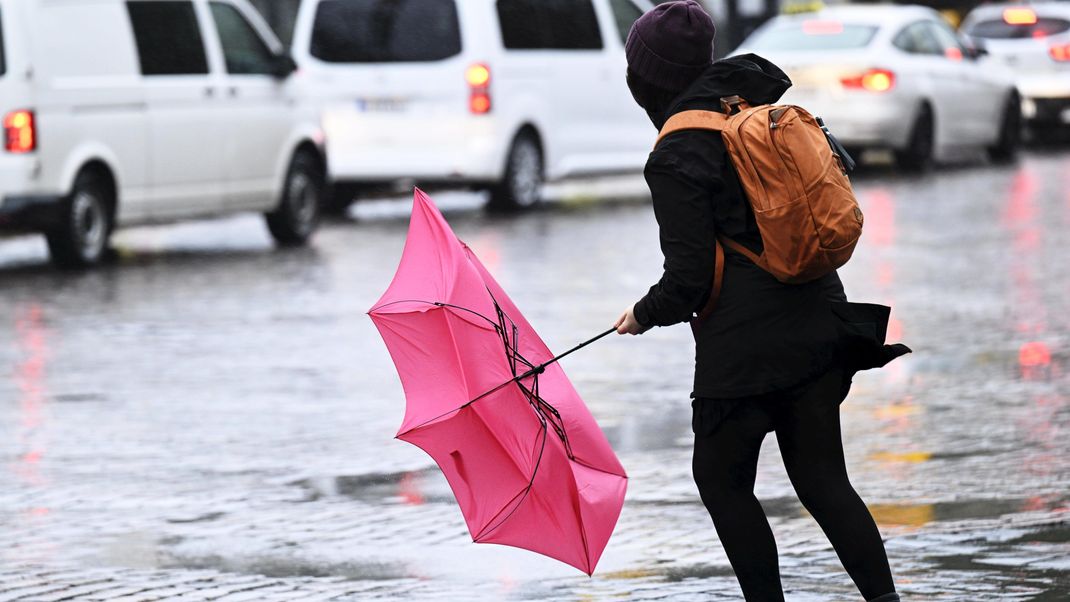 Eine Frau kämpft mit ihrem Regenschirm, der von einer Windböe bei Regen erfasst wird.