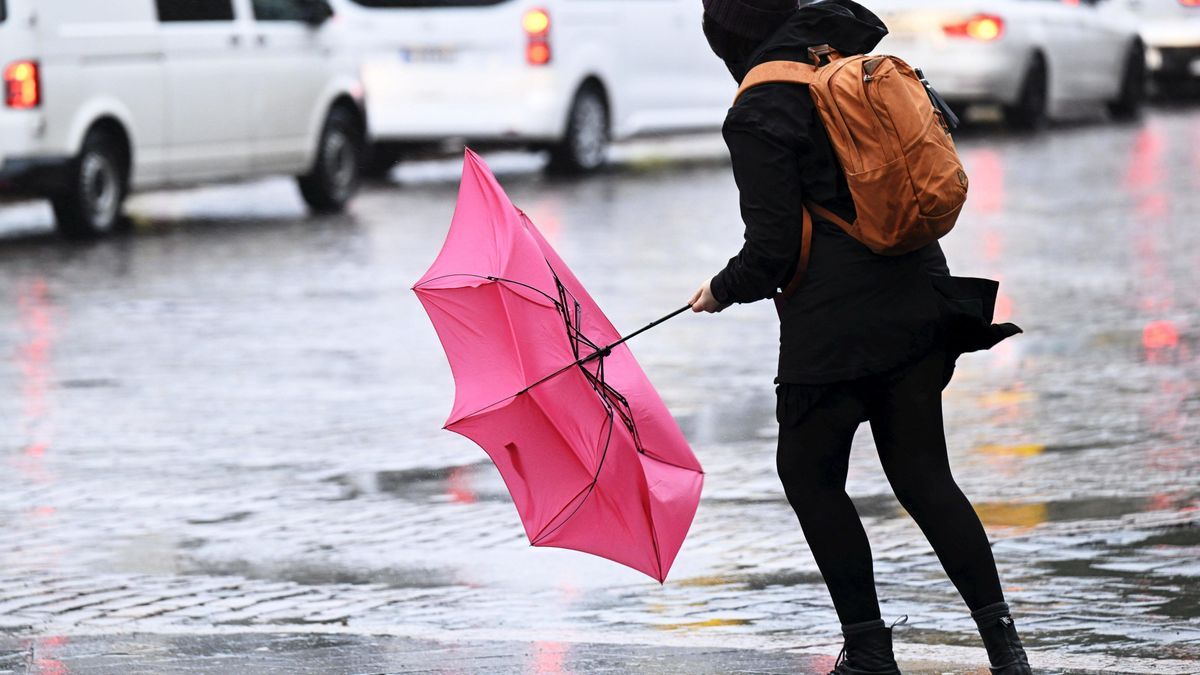 Eine Frau kämpft mit ihrem Regenschirm, der von einer Windböe bei Regen erfasst wird.