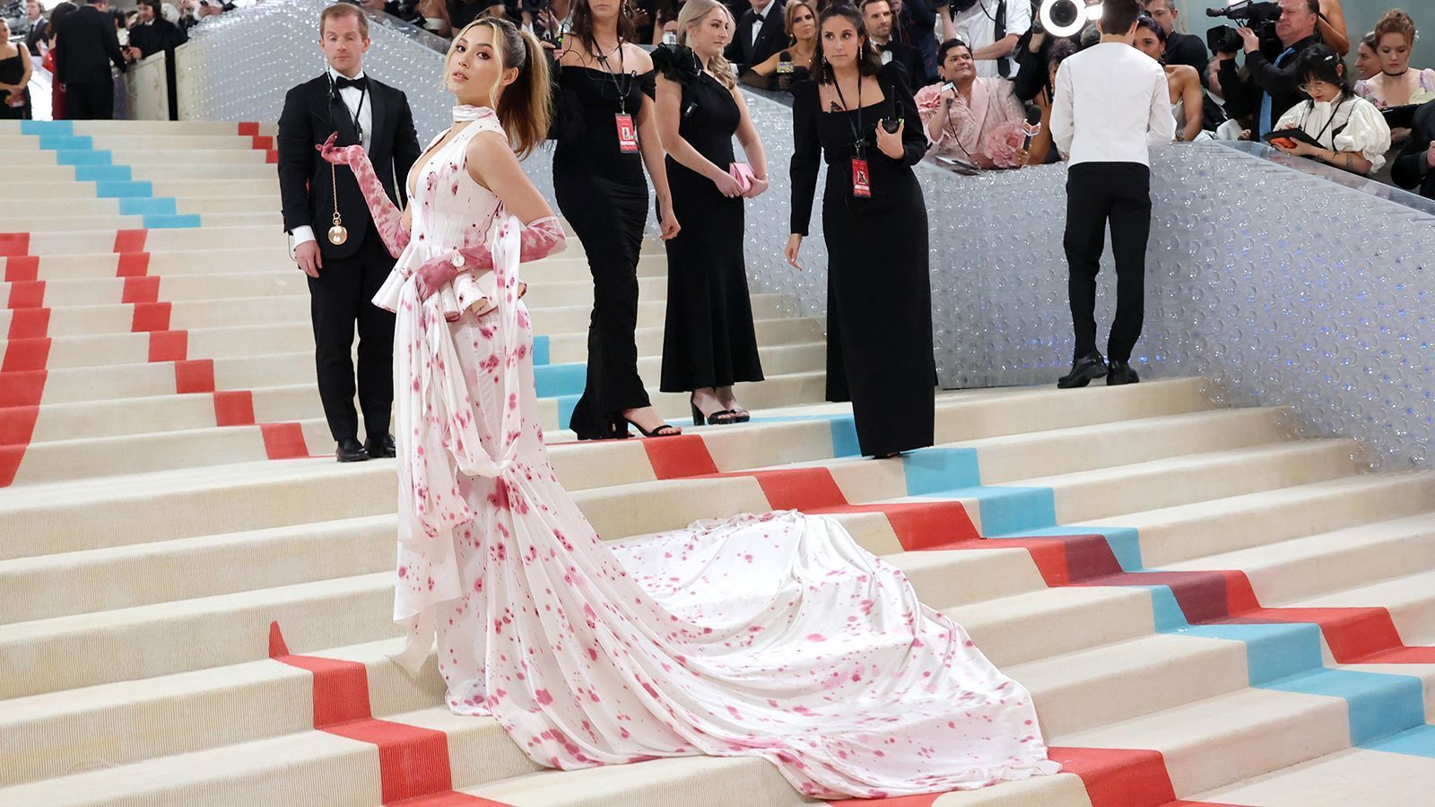 
                <strong>Eileen Gu</strong><br>
                Freestyle-Skierin Eileen Gu fällt nicht nur mit ihren Tricks im Schnee auf, auch auf der Met Gala setzte die erst 19-Jährige auf eine auffällige lange Robe. Die rot-rosa Schößchen auf dem Kleid erinnern an Rotweinflecken.  Das Kleid stammt aus der ersten Haute-Couture-Kollektion von Robert Wun, einem Designer aus Hongkong. Gu, die in den USA geboren wurde, startet seit 2019 für China. 2022 krönte sie sich zur Olympiasiegerin im Big Air.
              