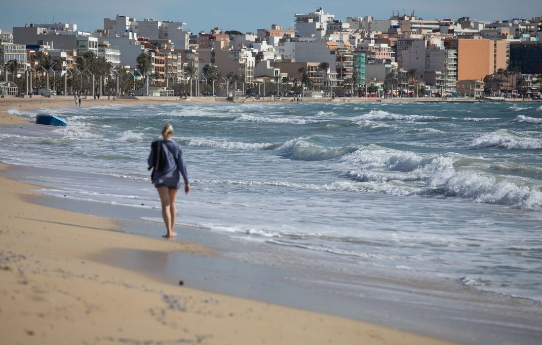 Eine Frau spaziert am Strand auf Mallorca entlang.