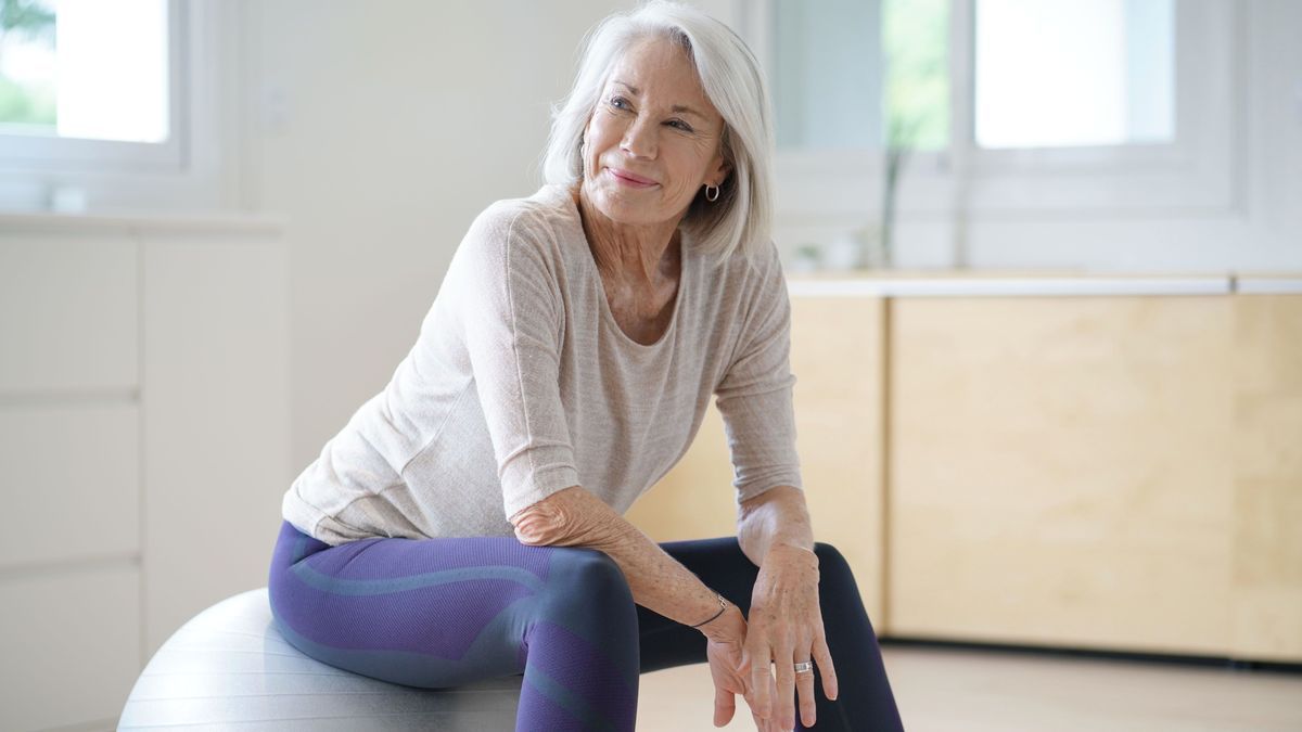Ältere Frau in den Wechseljahren/Menopause sitzt auf Ball in Fitnessstudio