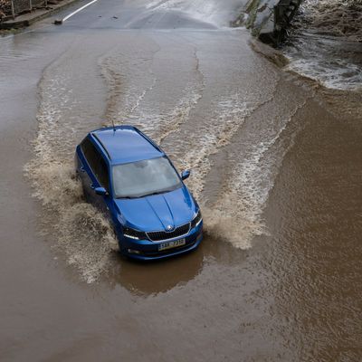 Ein Auto fährt über eine überschwemmte Straße. 