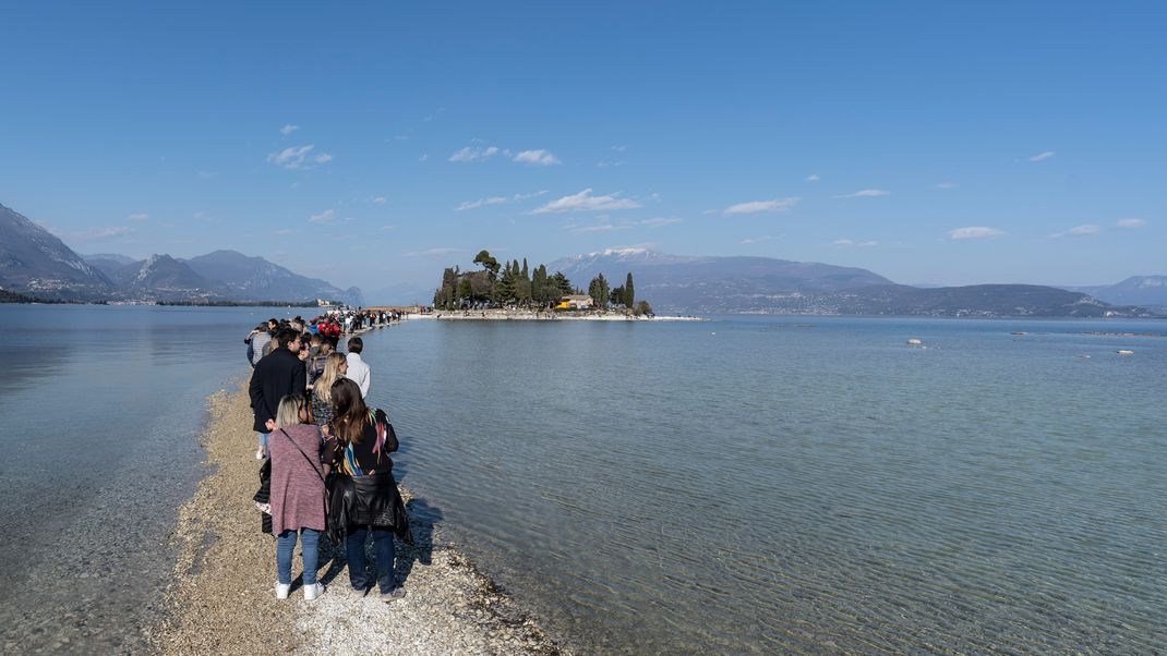 Menschen spazieren von Punta Belvedere nach Isola dei Conigli über den Gardasee aufgrund des ungewöhnlich niedrigen Wasserstands. Diese Insel auf dem Gardasee kann man eigentlich nur mit einem Boot erreichen.