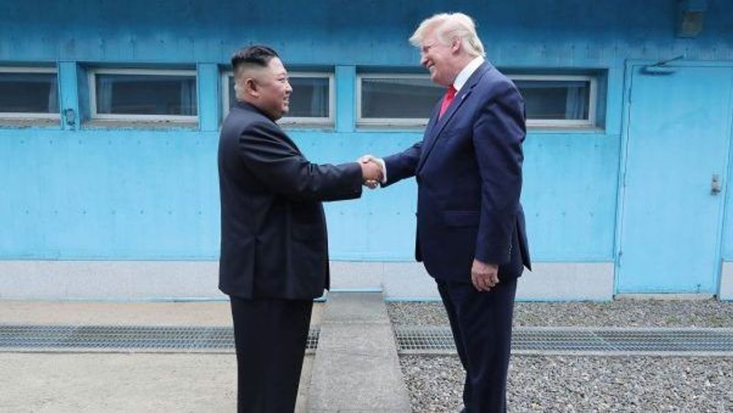 Nordkoreas Diktator Kim Jong-Un und der ehemalige US-Präsident Donald Trump reichen sich über die Demarkations-Linie zwischen Nord- und Südkorea die Hand. Die Grenze wurde 1953 beim Waffenstillstands-Abkommen im Korea-Krieg festgelegt.
