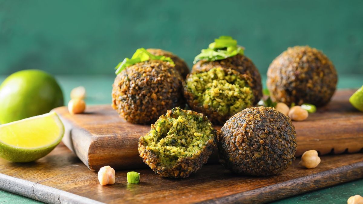 Board with tasty falafel balls and lime on color background