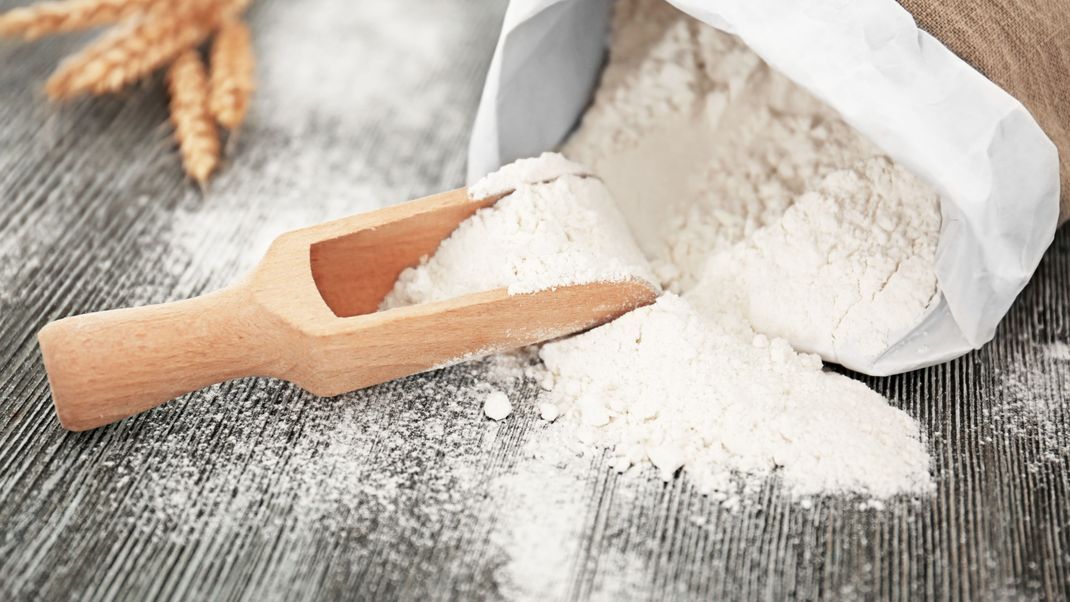 Bag and scoop with wheat flour on wooden table