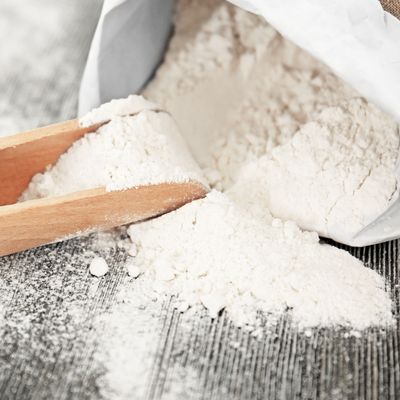 Bag and scoop with wheat flour on wooden table