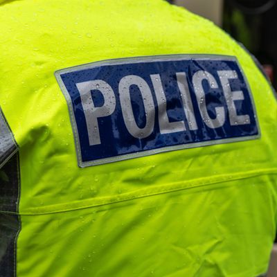 Rücken von Polizist mit neongelber Jacke mit der Aufschrift Police steht im Regen