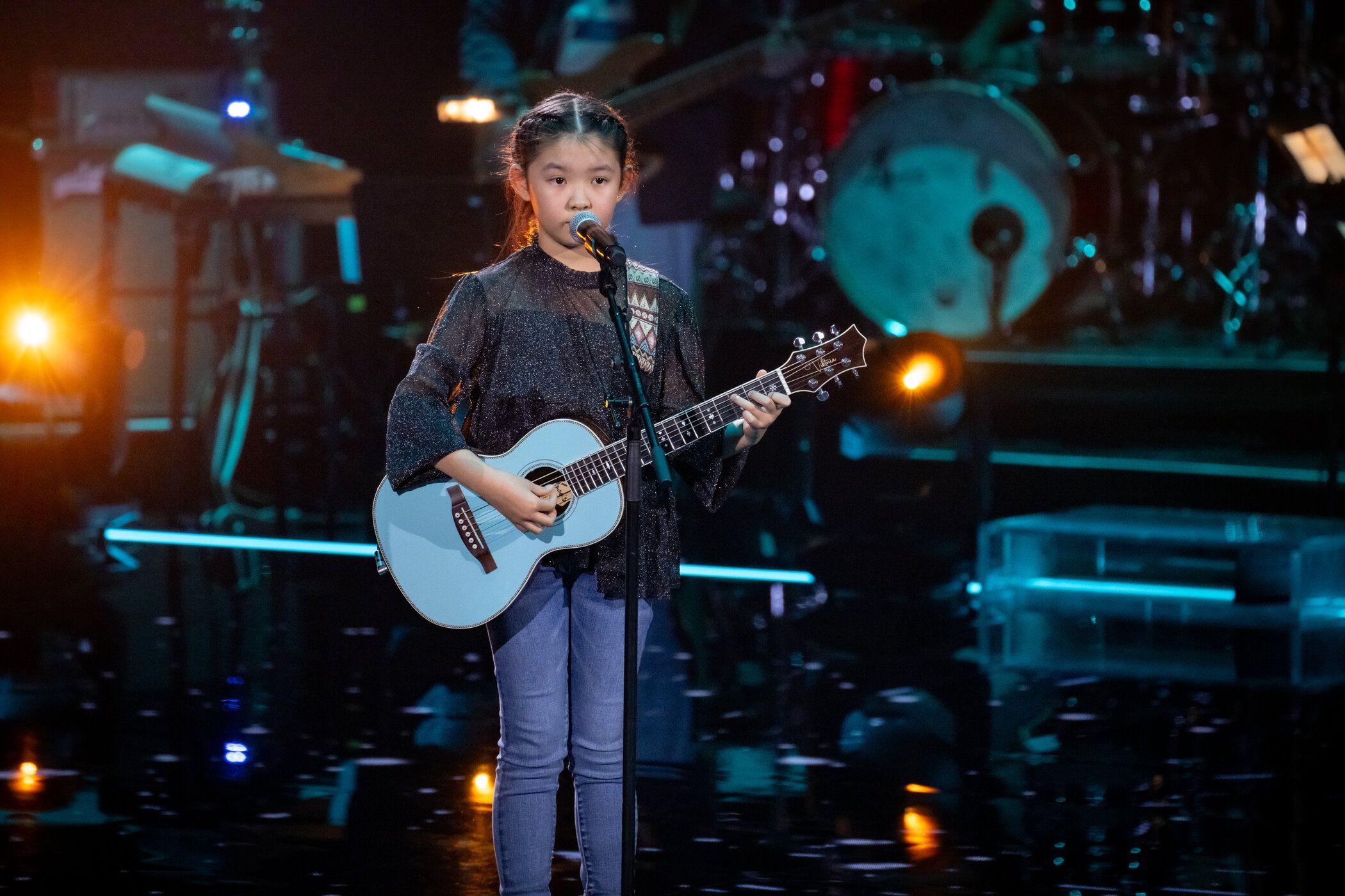 Viktoria steht mit ihrer blauen Gitarre auf der Bühne am Mikro.