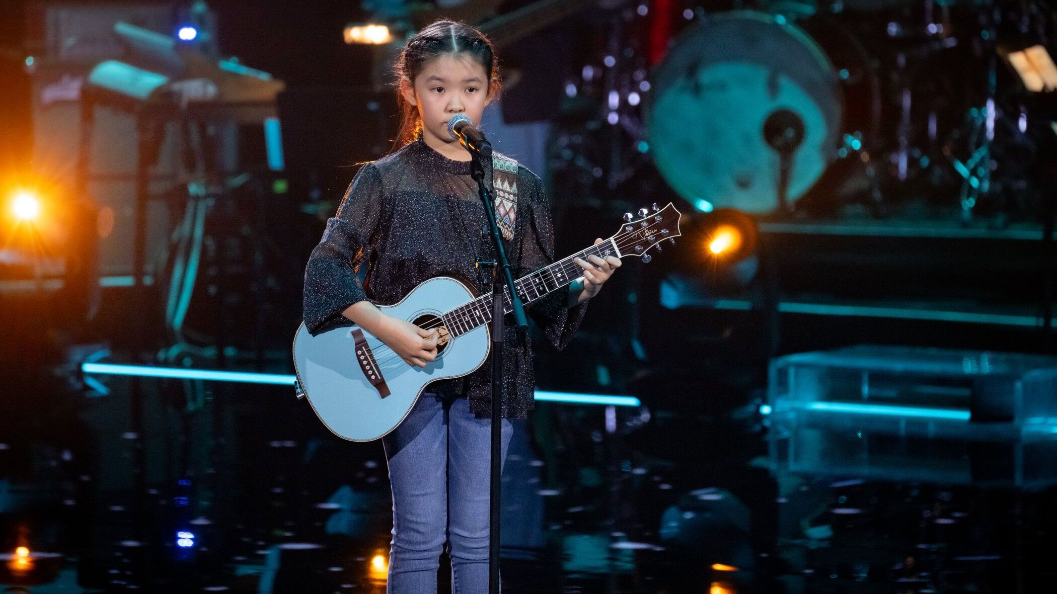 Viktoria steht mit ihrer blauen Gitarre auf der Bühne am Mikro.