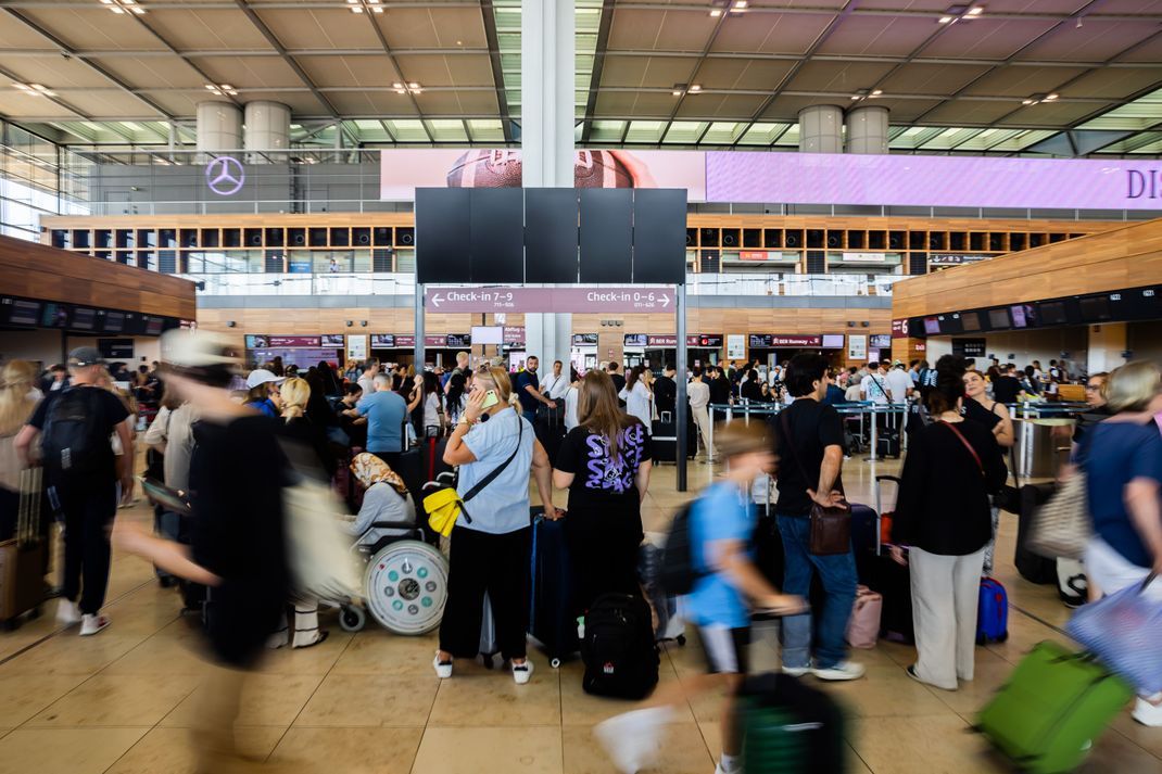 Zahlreiche Fluggäste warten am Hauptstadtflughafen Berlin Brandenburg vor einer schwarzen Anzeigetafel.