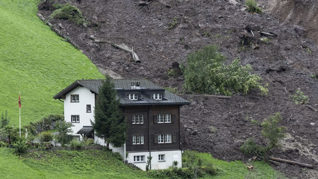 Schweiz, Schwanden: Geröll und Schlammmassen zeichnen das Gebiet hinter einem Haus nach einem Erdrutsch.