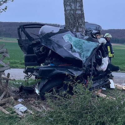 Einsatzkräfte der Feuerwehr gehen an einem zerstörten PKW entlang.