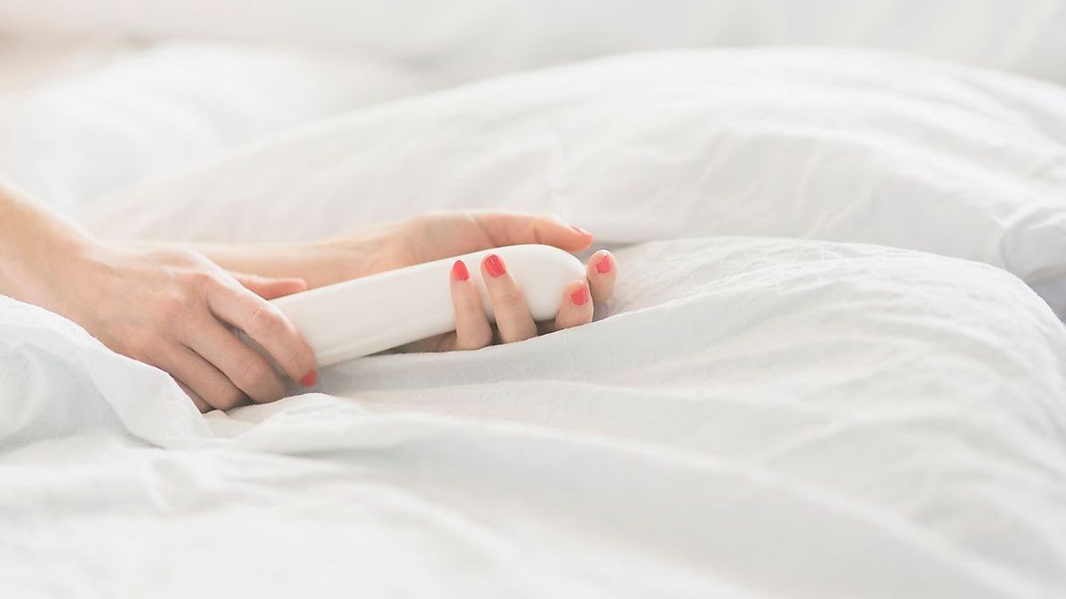 Hand of woman holding sex toy in bed