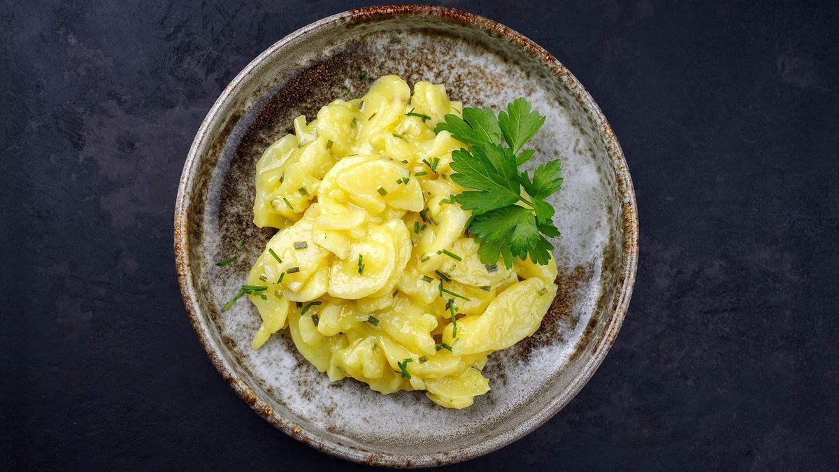 Traditional German potato salad with onion and chives served as top view in a design bowl on a black board