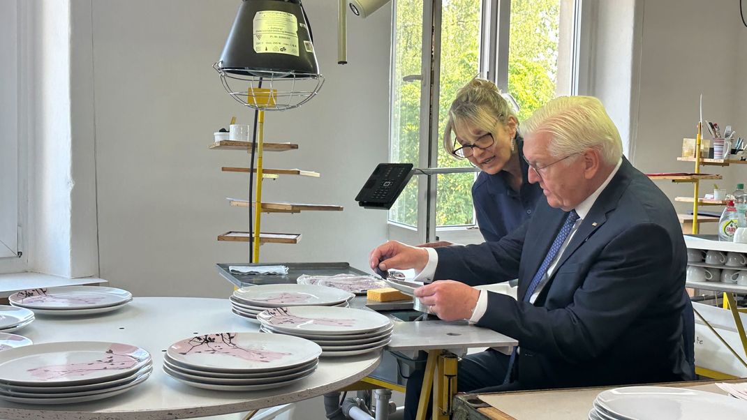 Bundespräsident Frank-Walter Steinmeier lässt sich bei seinem Besuch der Firma Seltmann in Weiden von Porzellandruckerin Mariella DeLuca die Dekoration eines Tellers erläutern.