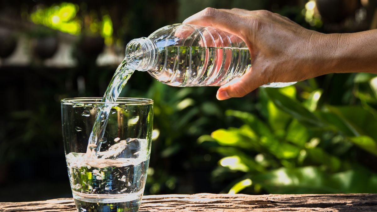 Female hand pouring water from bottle to glass on nature background