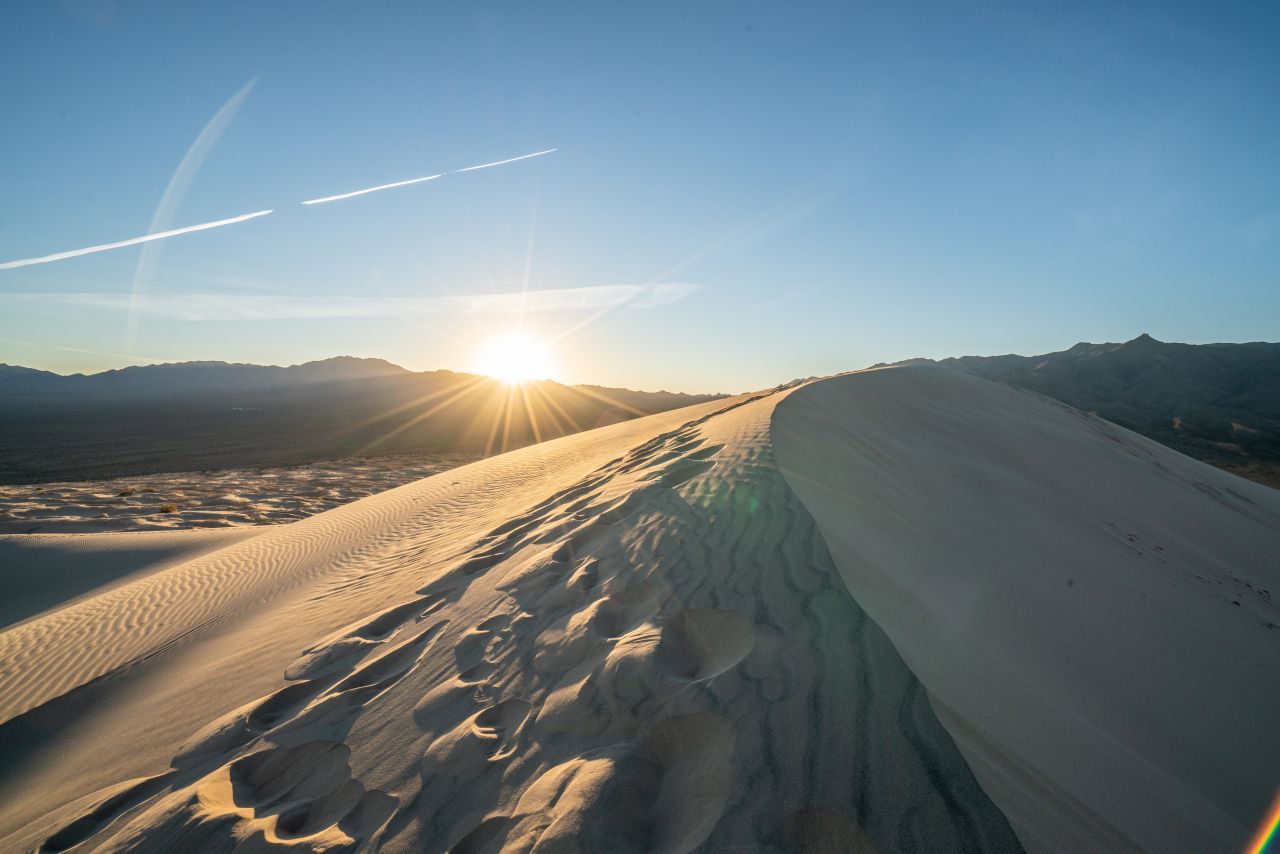 Kelso Dunes: Das Dünenfeld bedeckt eine Fläche von knapp 120 Quadratkilometern im Südwesten des Mojave National Preserve. Die bis zu 200 Meter hohen, "goldenen" Hügel sind im Lauf von 25.000 Jahren aus Sand entstanden, den der Wind vor allem aus dem ausgetrockneten Soda Lake herübergetragen hat. Und es handelt sich um "Singing Sand". Spaziert man durch die Dünen, lösen rieselnde Körnchen ein charakteristisches Brausen aus. Da