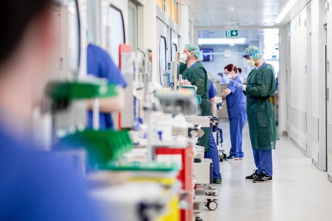 Krankenpfleger bekleiden sich mit Schutzkleidung vor dem Besuch in einem  Krankenzimmer.