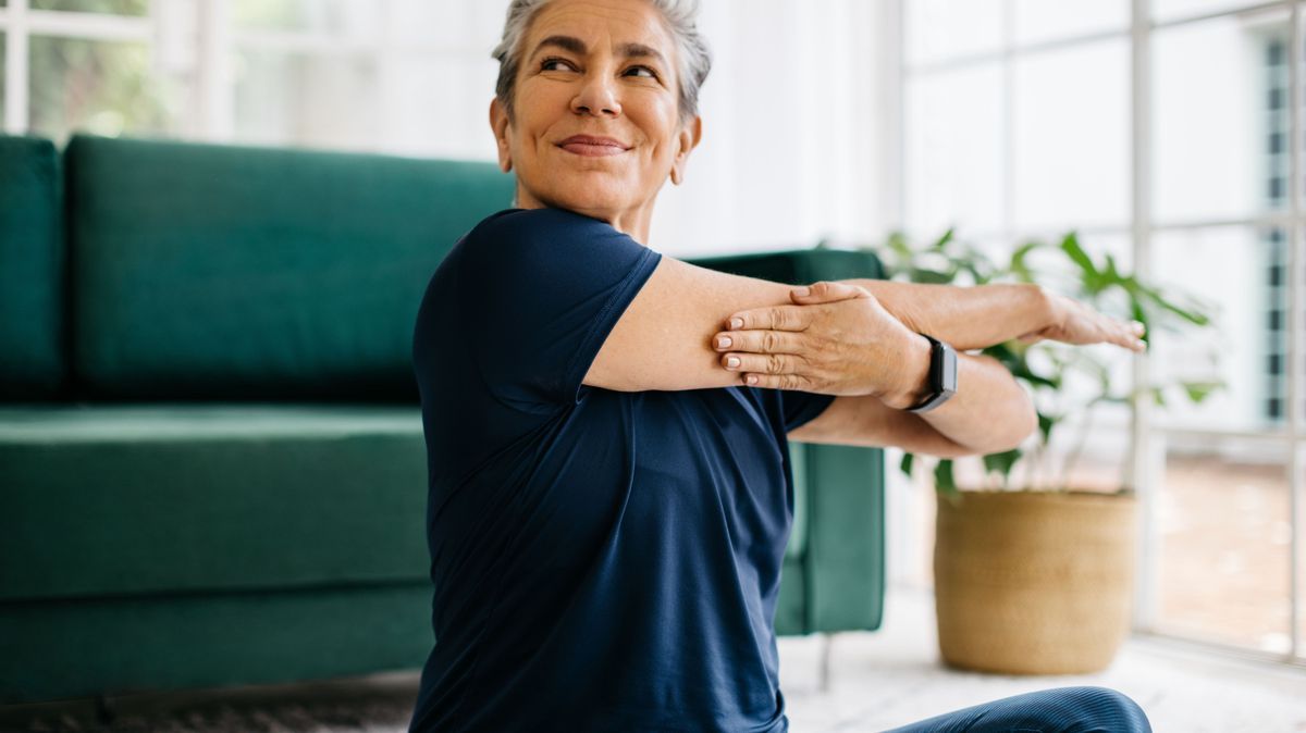 Happy and healthy senior woman doing a cross arm stretch in a peaceful yoga session at home