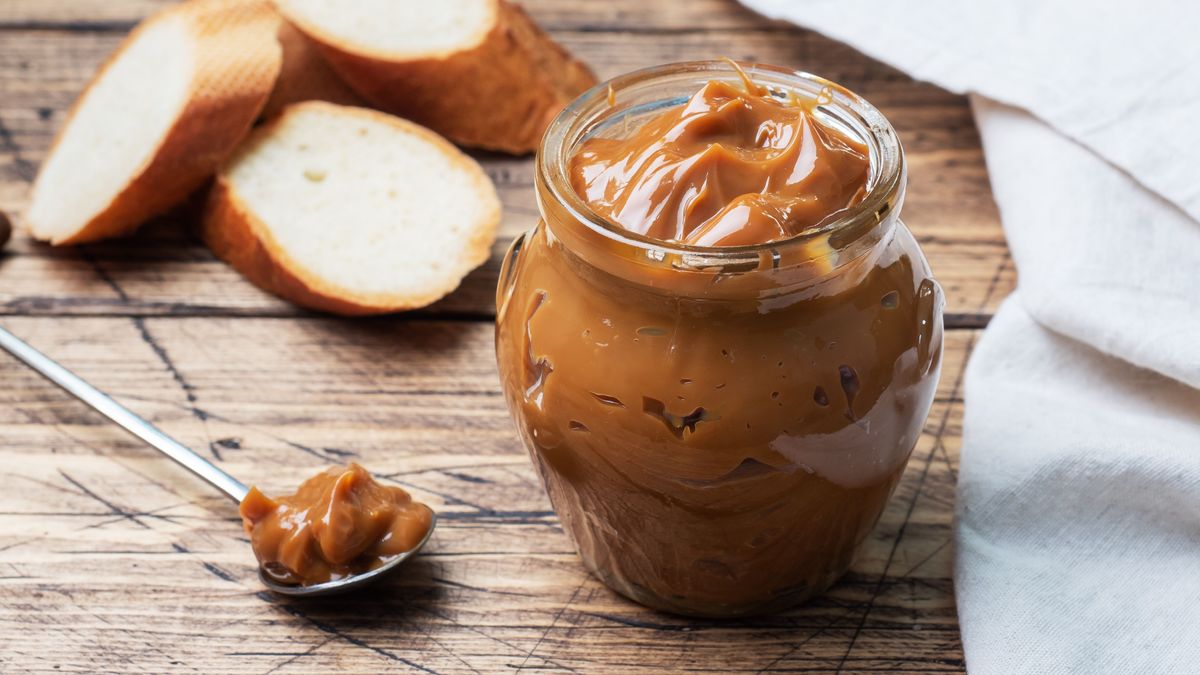 Boiled condensed milk with a glass jar on a wooden background. Sweet paste spread on slices of bread for Breakfast and dessert.