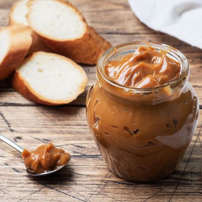 Boiled condensed milk with a glass jar on a wooden background. Sweet paste spread on slices of bread for Breakfast and dessert.