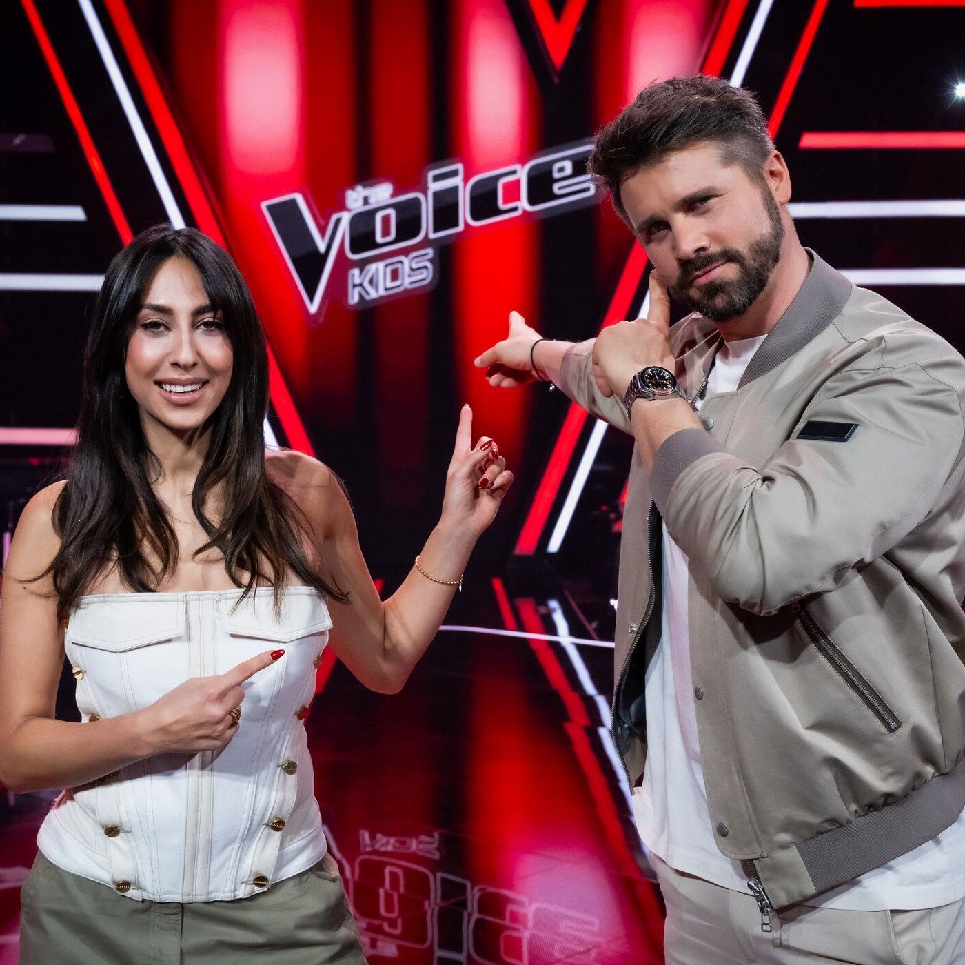 Melissa Khalaj und Thore Schölermann im "The Voice Kids"-Studio zeigen auf das Logo der Show