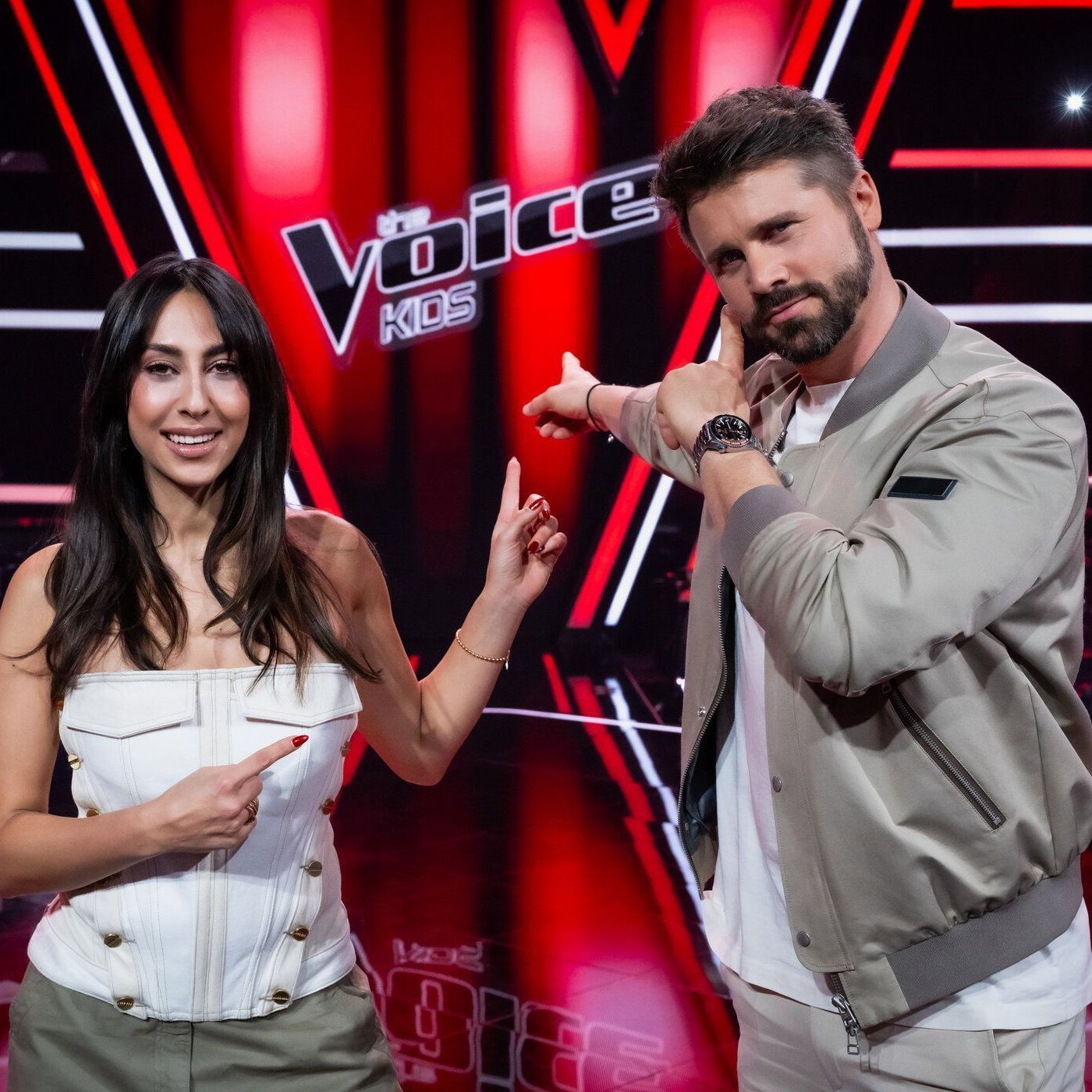 Melissa Khalaj und Thore Schölermann im "The Voice Kids"-Studio zeigen auf das Logo der Show