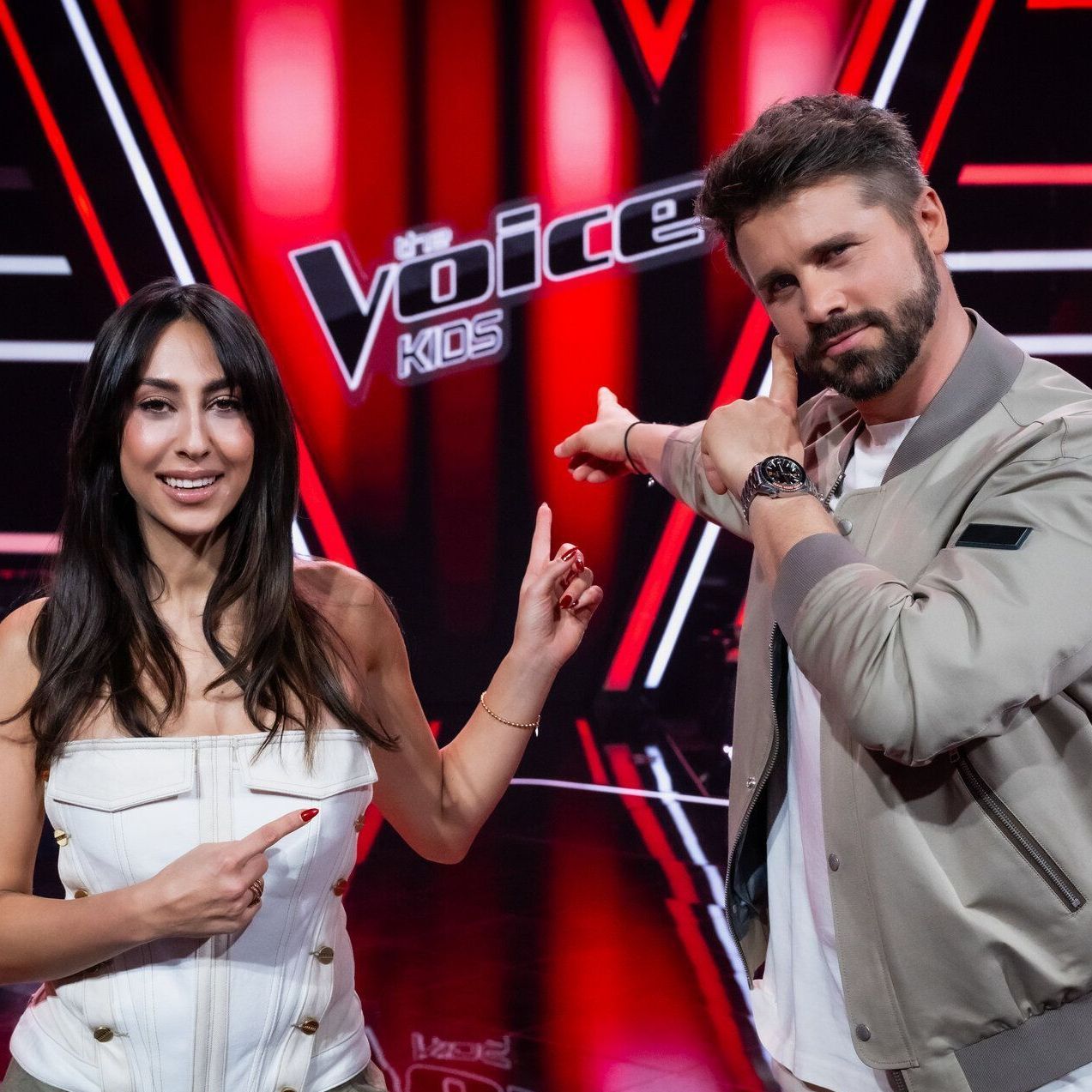 Melissa Khalaj und Thore Schölermann im "The Voice Kids"-Studio zeigen auf das Logo der Show