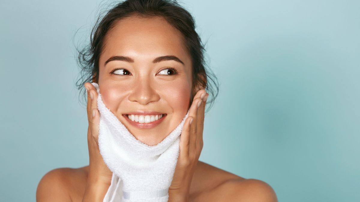 Woman cleaning facial skin with towel after washing face portrait. Beautiful happy smiling young asian female model wiping facial skin with soft towel, removing makeup. High quality studio shot