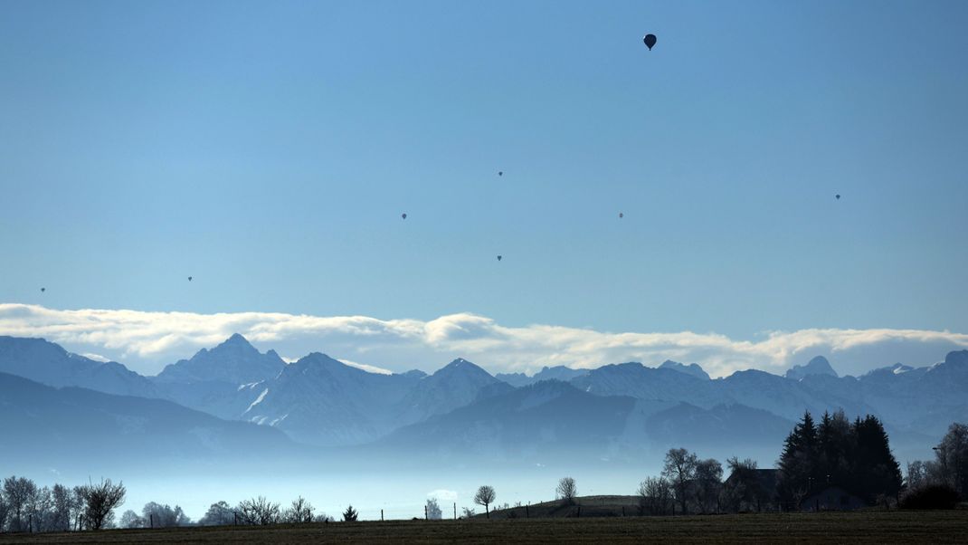 Heißluftballons sind am strahlend blauem Himmel über dem Panorama der Alpen zu sehen.